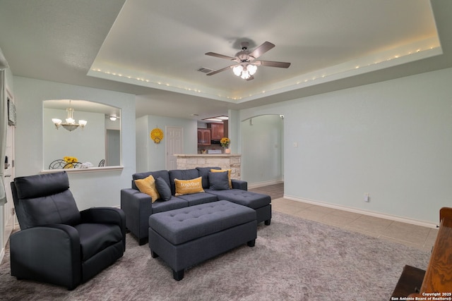 living room featuring a raised ceiling, light tile patterned flooring, and ceiling fan with notable chandelier