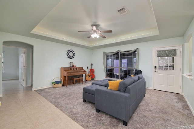 tiled living room with ceiling fan and a tray ceiling