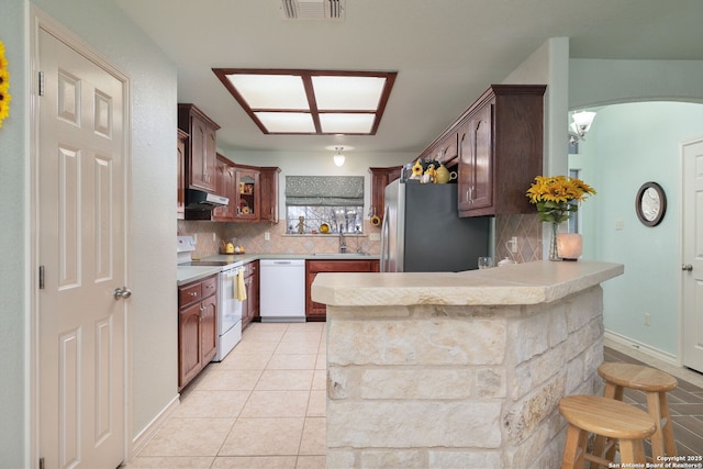 kitchen featuring a kitchen bar, decorative backsplash, kitchen peninsula, white appliances, and sink