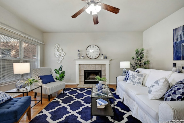 living room with a tiled fireplace, wood-type flooring, and ceiling fan