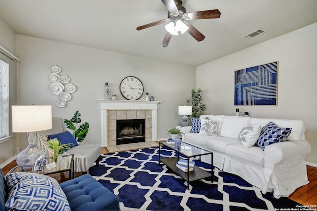 living room featuring a tiled fireplace, wood-type flooring, and ceiling fan