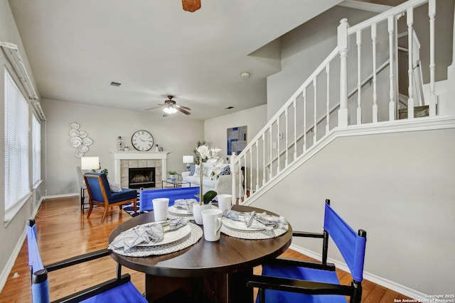 dining area with hardwood / wood-style flooring, a tiled fireplace, and ceiling fan