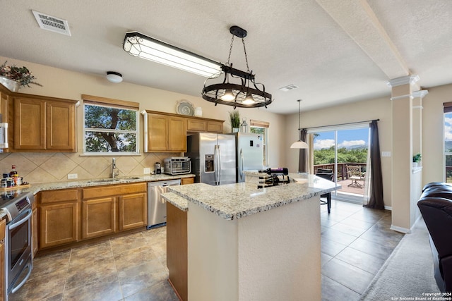 kitchen with pendant lighting, backsplash, sink, light stone countertops, and stainless steel appliances