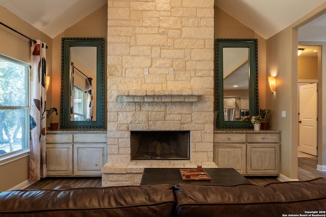 living room with vaulted ceiling and a stone fireplace