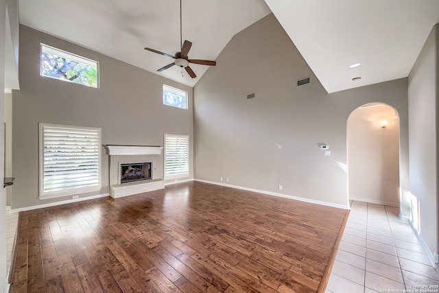 unfurnished living room with a brick fireplace, light wood-type flooring, high vaulted ceiling, and ceiling fan