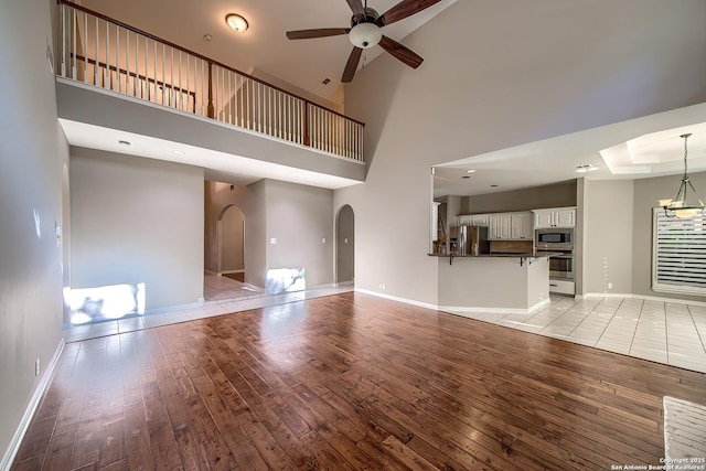 unfurnished living room with ceiling fan with notable chandelier, a high ceiling, and light wood-type flooring