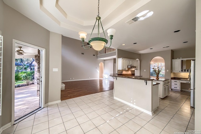 kitchen featuring white cabinetry, stainless steel fridge, pendant lighting, light tile patterned floors, and ceiling fan with notable chandelier