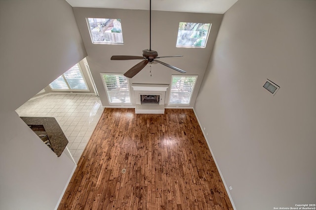 unfurnished living room with hardwood / wood-style floors, ceiling fan, and a high ceiling