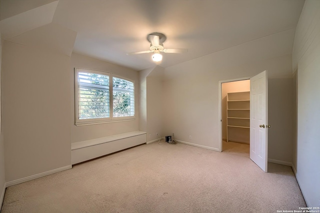 unfurnished bedroom with a closet, light colored carpet, a spacious closet, and ceiling fan