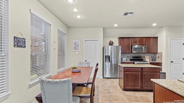 kitchen with backsplash, light stone counters, light tile patterned flooring, and stainless steel appliances