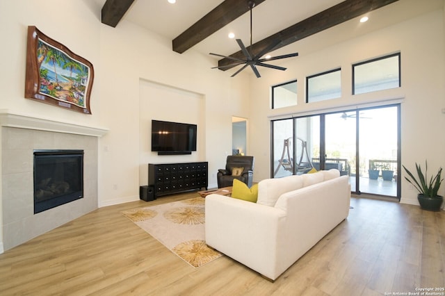 living room with a tile fireplace, ceiling fan, beamed ceiling, and light hardwood / wood-style floors