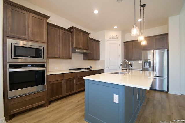 kitchen featuring pendant lighting, a center island with sink, sink, decorative backsplash, and stainless steel appliances