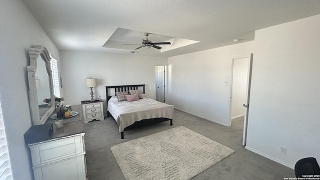 bedroom featuring a tray ceiling, dark carpet, and ceiling fan