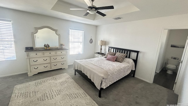 bedroom with ceiling fan, dark carpet, and a tray ceiling