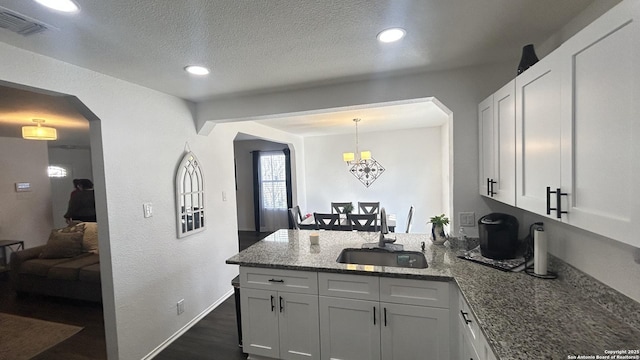 kitchen featuring light stone countertops, sink, an inviting chandelier, white cabinets, and hanging light fixtures