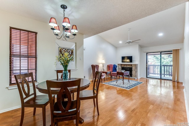 dining space with a fireplace, light wood-style flooring, ceiling fan with notable chandelier, baseboards, and vaulted ceiling