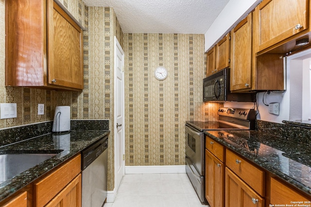kitchen featuring baseboards, wallpapered walls, a textured ceiling, dark stone countertops, and stainless steel appliances