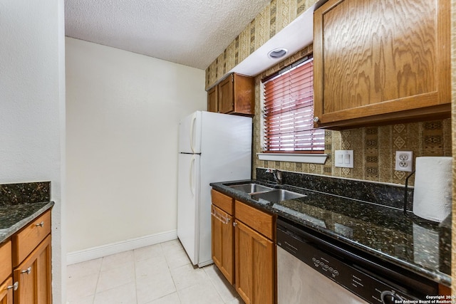 kitchen with stainless steel dishwasher, a sink, a textured ceiling, and dark stone countertops