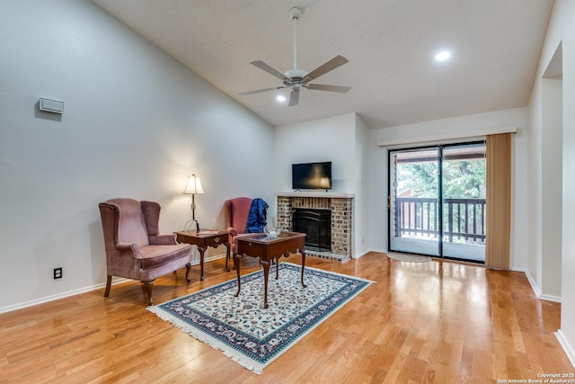 living area featuring a ceiling fan, baseboards, light wood-style flooring, and a fireplace