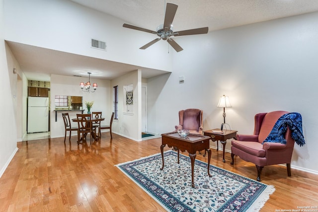 living area featuring high vaulted ceiling, light wood-style flooring, ceiling fan with notable chandelier, baseboards, and visible vents