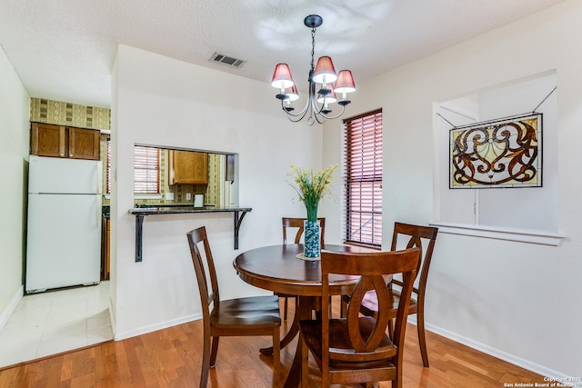 dining room with visible vents, light wood-style floors, baseboards, and a notable chandelier