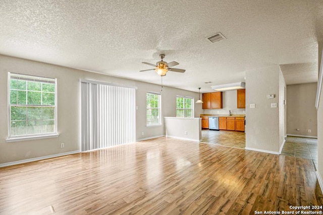 unfurnished living room with a textured ceiling, light hardwood / wood-style floors, a wealth of natural light, and ceiling fan