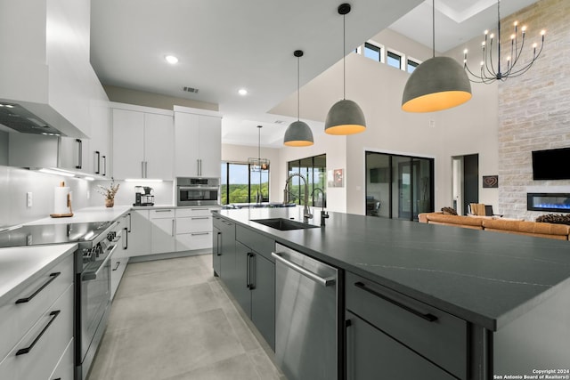 kitchen featuring a large island with sink, white cabinets, hanging light fixtures, sink, and wall chimney exhaust hood