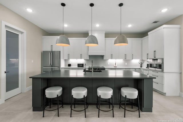 kitchen with a center island with sink, white cabinetry, sink, and stainless steel refrigerator