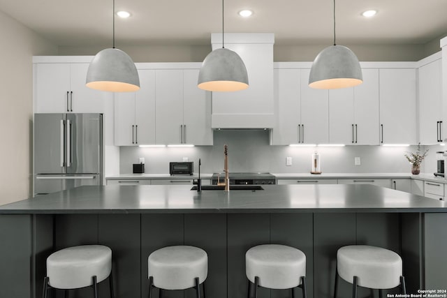 kitchen with pendant lighting, white cabinetry, stainless steel refrigerator, and a kitchen island with sink