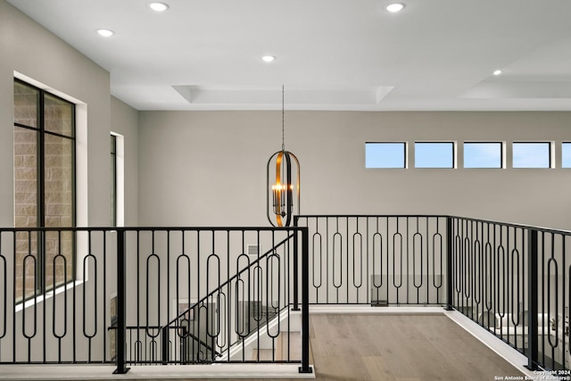 corridor featuring a tray ceiling, an inviting chandelier, and light wood-type flooring