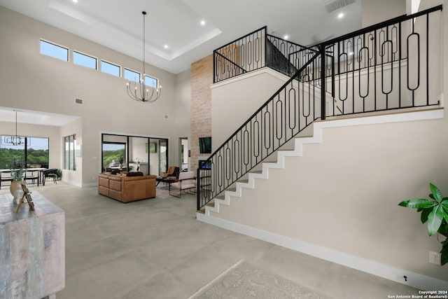 stairs featuring concrete flooring, a high ceiling, a raised ceiling, and a notable chandelier