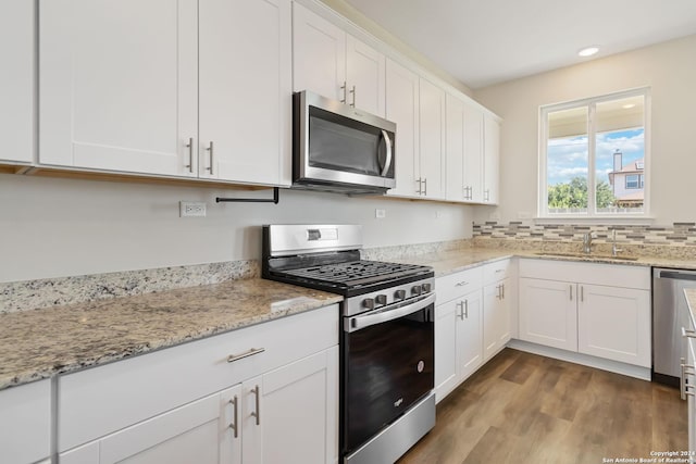 kitchen featuring dark wood-type flooring, sink, light stone counters, stainless steel appliances, and white cabinets