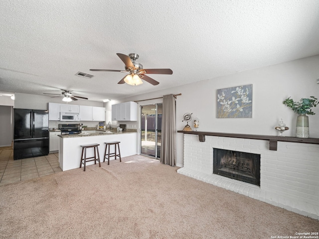 living room featuring ceiling fan, sink, a brick fireplace, a textured ceiling, and light carpet