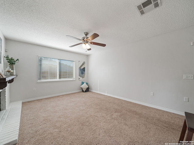 spare room with light carpet, ceiling fan, a textured ceiling, and a brick fireplace