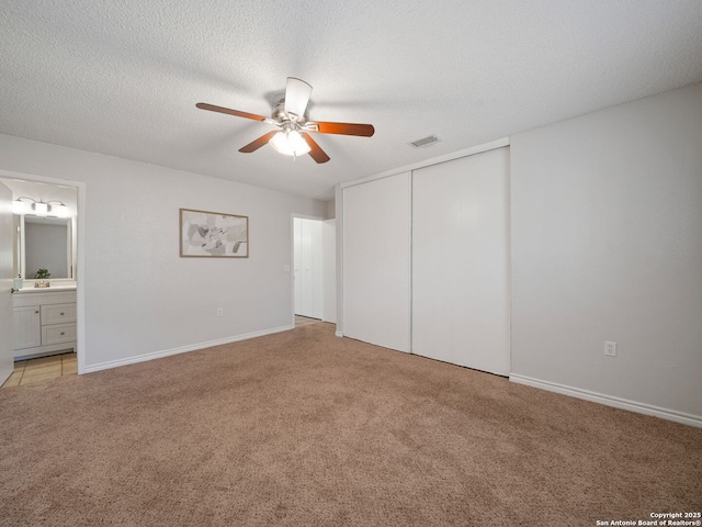 unfurnished bedroom with light carpet, ensuite bath, a textured ceiling, ceiling fan, and a closet