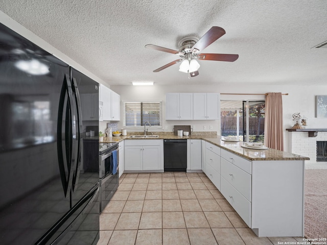 kitchen featuring kitchen peninsula, a brick fireplace, sink, black appliances, and white cabinetry