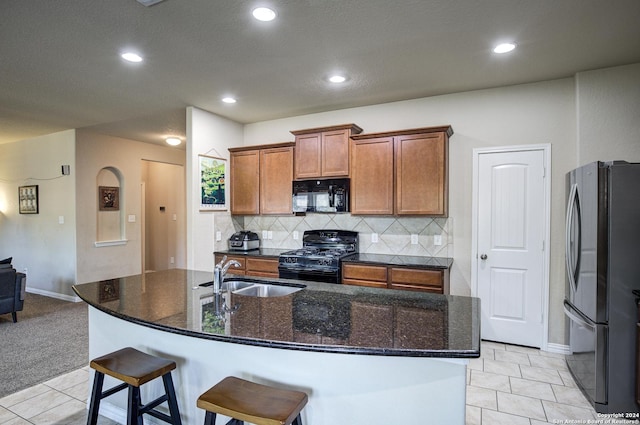 kitchen with light tile patterned flooring, sink, an island with sink, and black appliances