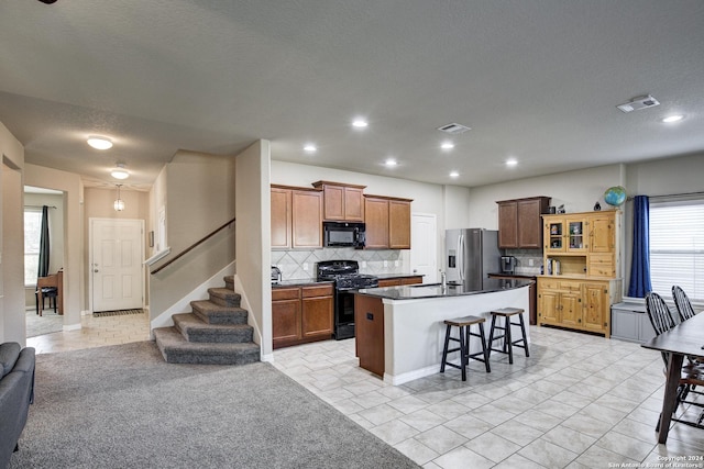 kitchen with a kitchen breakfast bar, backsplash, black appliances, light tile patterned floors, and a center island with sink