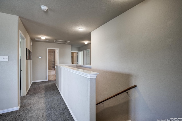 hallway with a textured ceiling and dark colored carpet