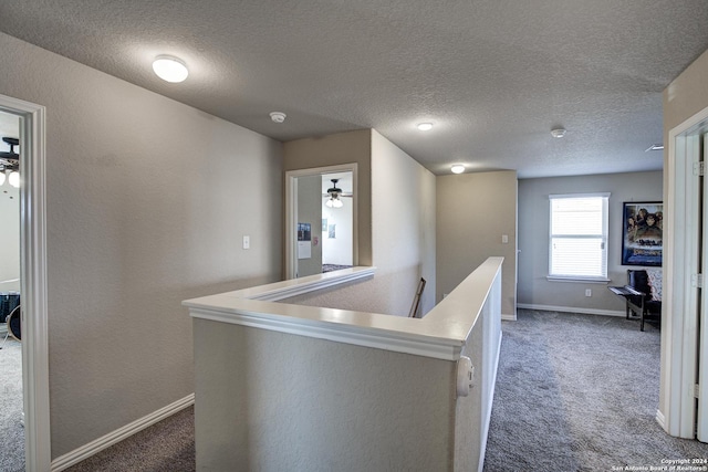 hall featuring a textured ceiling and dark colored carpet