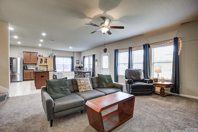 living room featuring light carpet, a textured ceiling, ceiling fan, and a healthy amount of sunlight