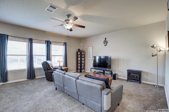 carpeted living room with a textured ceiling, a wood stove, and ceiling fan