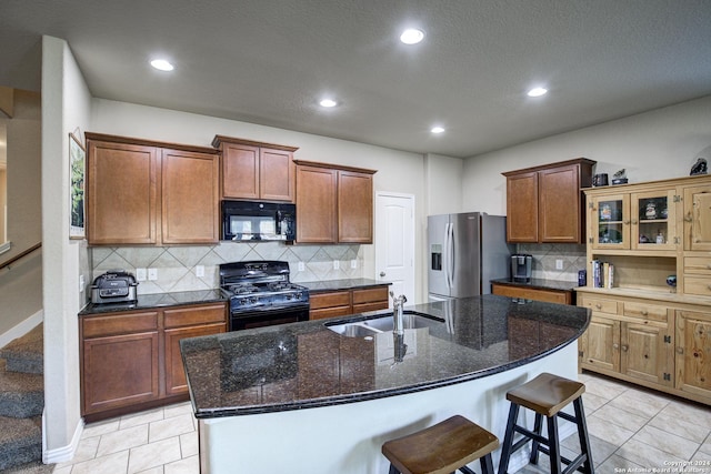 kitchen with light tile patterned flooring, sink, a center island with sink, and black appliances