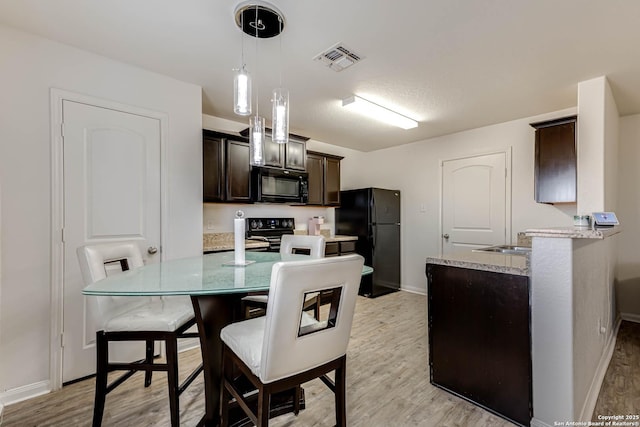 kitchen with dark brown cabinets, light wood-type flooring, hanging light fixtures, and black appliances