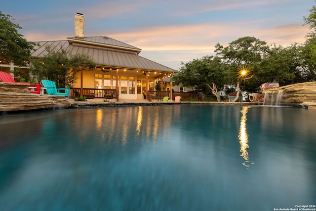 pool at dusk with ceiling fan and a patio