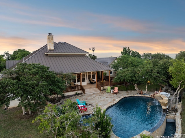 pool at dusk with pool water feature and a patio area