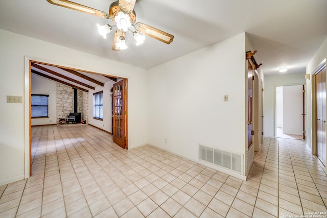 unfurnished room with lofted ceiling with beams, ceiling fan, and a wood stove