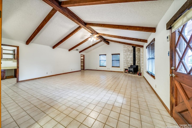 unfurnished living room featuring a wood stove, ceiling fan, lofted ceiling with beams, and a textured ceiling