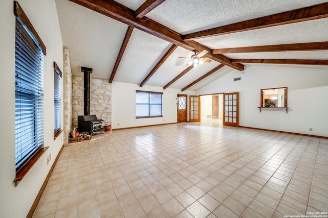 unfurnished living room with a wood stove, lofted ceiling with beams, ceiling fan, a textured ceiling, and light tile patterned flooring