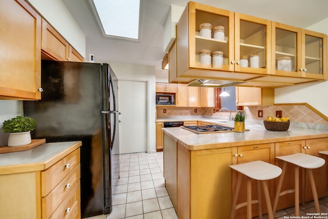 kitchen featuring black appliances, a skylight, decorative backsplash, light tile patterned flooring, and kitchen peninsula